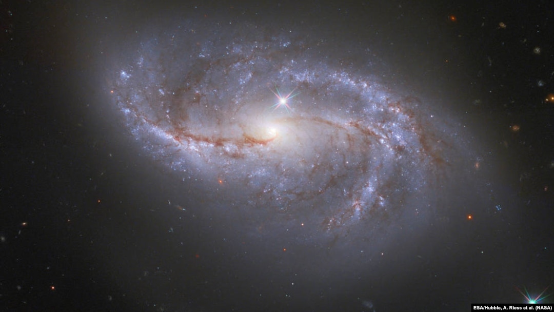 Gledajući duboko u svemir, NASA/ESA Hubble svemirski teleskop hvata usputni pogled na brojne strukture nalik na ruke koje se prostiru oko ove spiralne galaksije sa prečkama, poznate kao NGC 2608.