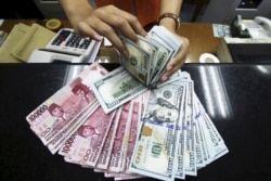 Seorang teller di tempat penukaran uang menunjukkan Rupiah dan dolar AS di Jakarta, 12 Agustus 2015. (Foto: Antara via Reuters)