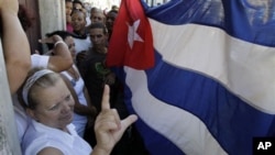 Laura Pollan, leader of Cuba's dissident group Ladies in White, makes an "L" referring to the Spanish word for Freedom, "Libertad" as supporters of Cuba's government hold up a Cuban flag during in Havana, Cuba. (file)