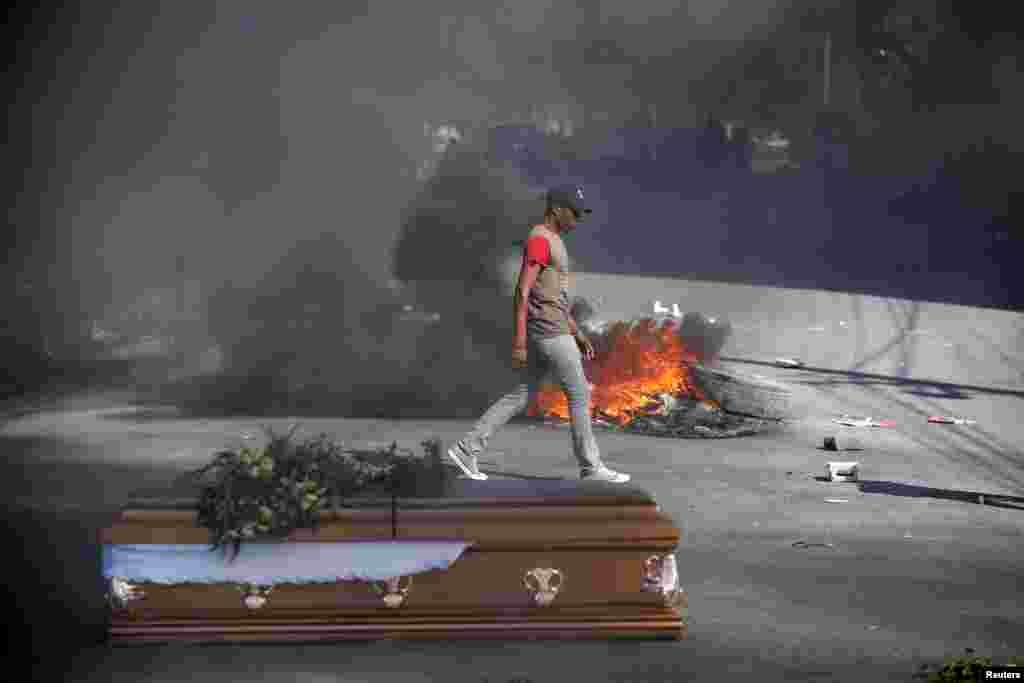 A man walks past burning tires and one of the caskets of victims of anti-government protests, placed in the street by relatives and fellow demonstrators, in Port-au-Prince, Haiti, March 4, 2019.