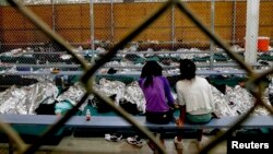 Two young girls watch a World Cup soccer match on a television from their holding area at a detention facility in Nogales, Arizona.