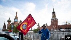 Seorang pria berpose dengan bendera merah di depan Lapangan Merah dalam peringatan 75 tahun kekalahan Nazi dalam Perang Dunia Kedua di Moskow, Rusia, 9 Mei 2020.