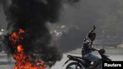 Seorang pria memberi hormat tiga jari saat melewati ban yang terbakar saat memprotes kudeta militer, di Mandalay, Myanmar 1 April 2021. (Foto: Reuters)