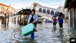 FILE - People wade through high tide near the Rialto Bridge in Venice, Italy, Dec. 23, 2019. Winds pushed 1.87 meters of water into the city, producing its second-worst flood in history; four more floods over the next six weeks triggered fears about worsening climate change.