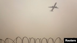 FILE - A plane flies in the polluted air above the airport fences in Beijing, Feb. 22, 2012. An IATAA official says a deal on limiting carbon dioxide emissions from aviation will likely be reached next year.