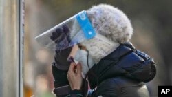 A woman wearing a face mask and face shield get ready for her routine COVID-19 throat swab at a coronavirus testing site in Beijing, Dec. 7, 2022. 