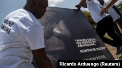 Des hommes placent un portrait du défunt président haïtien Jovenel Moïse avec une citation de lui qui se lit en créole "J'ai essayé, n'abandonnez pas. Continuez la bataille" à un mémorial devant le Palais présidentiel, à Port-au-Prince, Haïti le 14 juillet 2021.