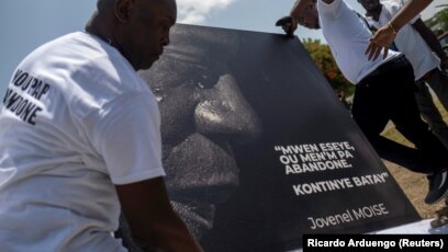 Des hommes placent un portrait du défunt président haïtien Jovenel Moïse avec une citation de lui qui se lit en créole "J'ai essayé, n'abandonnez pas. Continuez la bataille" à un mémorial devant le Palais présidentiel, à Port-au-Prince, Haïti le 14 juillet 2021.