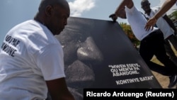 People place a portrait of late Haitian President Jovenel Moise with a quote from him that reads in creole "I try, you don't give up. Continue fighting" at a memorial outside the Presidential Palace, a week after his assassination, in Port-au-Prince, Haiti July 14, 2021.