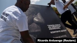 Des hommes placent un portrait du défunt président haïtien Jovenel Moïse avec une citation de lui qui se lit en créole "J'ai essayé, n'abandonnez pas. Continuez la bataille" à un mémorial devant le Palais présidentiel, à Port-au-Prince, Haïti le 14 juillet 2021.