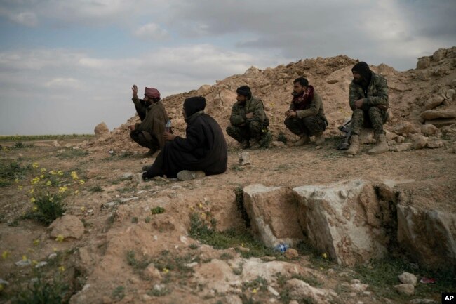 FILE - U.S.-backed Syrian Democratic Forces (SDF) fighters sit atop a hill in the desert outside the village of Baghoz, Syria, Feb. 14, 2019.