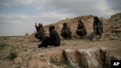 FILE - U.S.-backed Syrian Democratic Forces (SDF) fighters sit atop a hill in the desert outside the village of Baghuz, Syria, Feb. 14, 2019.