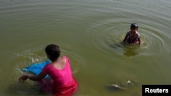 ARSIP – Seorang wanita mencuci pakaiannya dan putrinya mandi di Sungai Yamuna di hari yang panas di New Delhi, India, 24 April 2017 (foto: Reuters/Adnan Abidi)