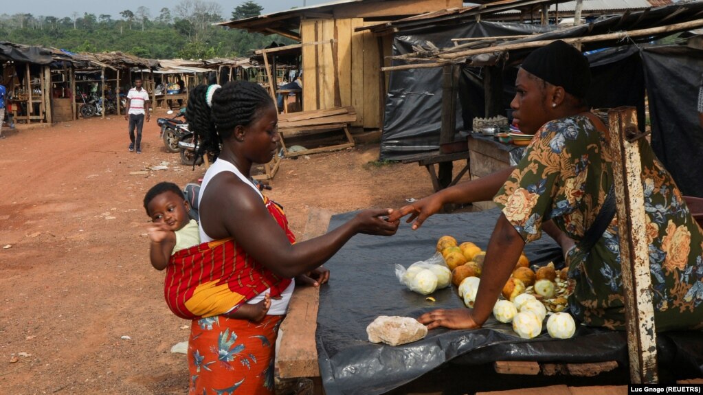 FILE - A woman buys fruit in the Ivorian cocoa farming village of Djigbadgi, commonly known as Bandikro or Bandit Town, located inside the Rapides Grah protected forest on January 7, 2021. (REUTERS/Luc Gnago)