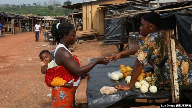 FILE - A woman buys fruit in the Ivorian cocoa farming village of Djigbadgi, commonly known as Bandikro or Bandit Town, located inside the Rapides Grah protected forest on January 7, 2021. (REUTERS/Luc Gnago)