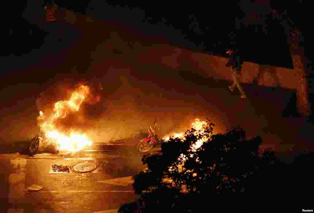 A motorcycle taxi driver walks past burning motorcycles set ablaze by anti-government demonstrators at Altamira Square in Caracas, Feb. 26, 2014.&nbsp;