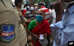 People wearing face masks as a precaution against the coronavirus wait to receive the second dose of the vaccine as an elderly woman pleads with a policeman to let her ahead of others at a public health center in Hyderabad, India, July 9, 2021.