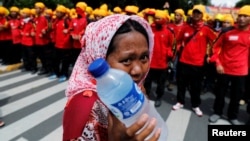 FILE - A street vendor holds drinking water as she walks near workers attending a May Day rally in front of presidential palace in Jakarta, Indonesia, May 1, 2016. 