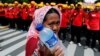 FILE - A street vendor holds drinking water as she walks near workers attending a May Day rally in front of presidential palace in Jakarta, Indonesia, May 1, 2016. 