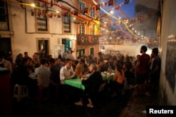 People sit outside in the Alfama neighborhood during the Festival of Popular Saints in Lisbon, Portugal, June 16, 2018.