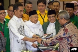 FILE - Indonesia's President Joko Widodo, front left, and the head of Indonesian Ulema Council Maruf Amin, center, submit their documents to election commission officials in Jakarta, Aug. 10, 2018, during their registration for the 2019 presidential election.