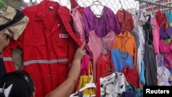 FILE -- A customer looks at PDVSA overalls for sale at a market in Maracaibo, Venezuela, Sept. 11, 2016.