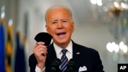 President Joe Biden holds up his face mask as he speaks about the COVID-19 pandemic during a prime-time address from the East Room of the White House, March 11, 2021.