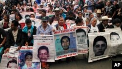FILE - Relatives of 43 missing students missing since they were taken by local police in September 2014 hold photos of their loved ones, April 24, 2016. Mexico's President Enrique Pena Nieto signed a law Thursday aimed at addressing the country's unsolved disappearances by creating a National Search System with local branches in the states.