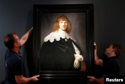 Gallery assistants hold a Rembrandt painting called "Portrait of a Young Man" at Hermitage Amsterdam in the Netherlands capital, May 16, 2018.