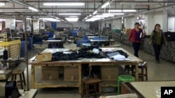 FILE - Workers walk past idle machinery as they strike at the Cuiheng Handbag Factory in Nanlang township in Zhongshan city in southern China's Guangdong Province, March 26, 2015.