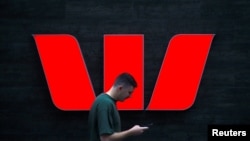 A pedestrian looks at his phone as he walks past a logo for Australia's Westpac Banking Corp located outside a branch in central Sydney, Australia, November 5, 2018. REUTERS/David Gray