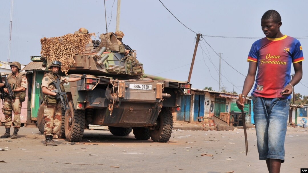 A young anti-Balaka Christian militiaman carrying a machete walks by French soldiers taking part in 'Operation Sangaris' and standing guard at the PK 12 crossroad in Bangui, Jan. 23, 2014.