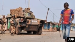 A young anti-Balaka Christian militiaman carrying a machete walks by French soldiers taking part in 'Operation Sangaris' and standing guard at the PK 12 crossroad in Bangui, Jan. 23, 2014.