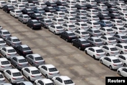 FILE - A man walks among cars which are ready for export at the port of Taipei, northern Taiwan, April 16, 2014.