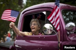 A woman waves an American flag as she rides in an antique pickup truck through Barnstable Village on Massachusetts' Cape Cod during the community's annual Independence Day parade, July 4, 2015.