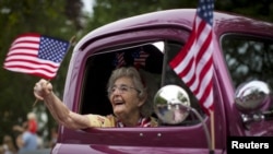 FILE - A woman waves an American flag as she rides in an antique pickup truck through Barnstable Village on Massachusetts' Cape Cod during the community's annual Independence Day parade, July 4, 2015. 