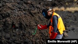 A scientist with the Canary Islands' volcanology institute, Involcan, measures the temperature of a lava, or melted rock from a volcano, flow on the Canary island of La Palma, Spain, on October 30, 2021. (AP Photo/Emilio Morenatti)