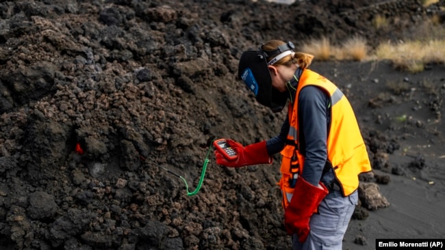 A scientist with the Canary Islands' volcanology institute, Involcan, measures the temperature of a lava, or melted rock from a volcano, flow on the Canary island of La Palma, Spain, on October 30, 2021. (AP Photo/Emilio Morenatti)