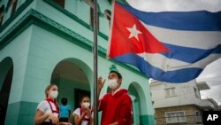 Estudiantes, con mascarilla por la pandemia del coronavirus, arrían una bandera cubana para evitar que se moje por la lluvia durante el primer día de escuela presencial en meses, en La Habana, el 8 de noviembre de 2021.