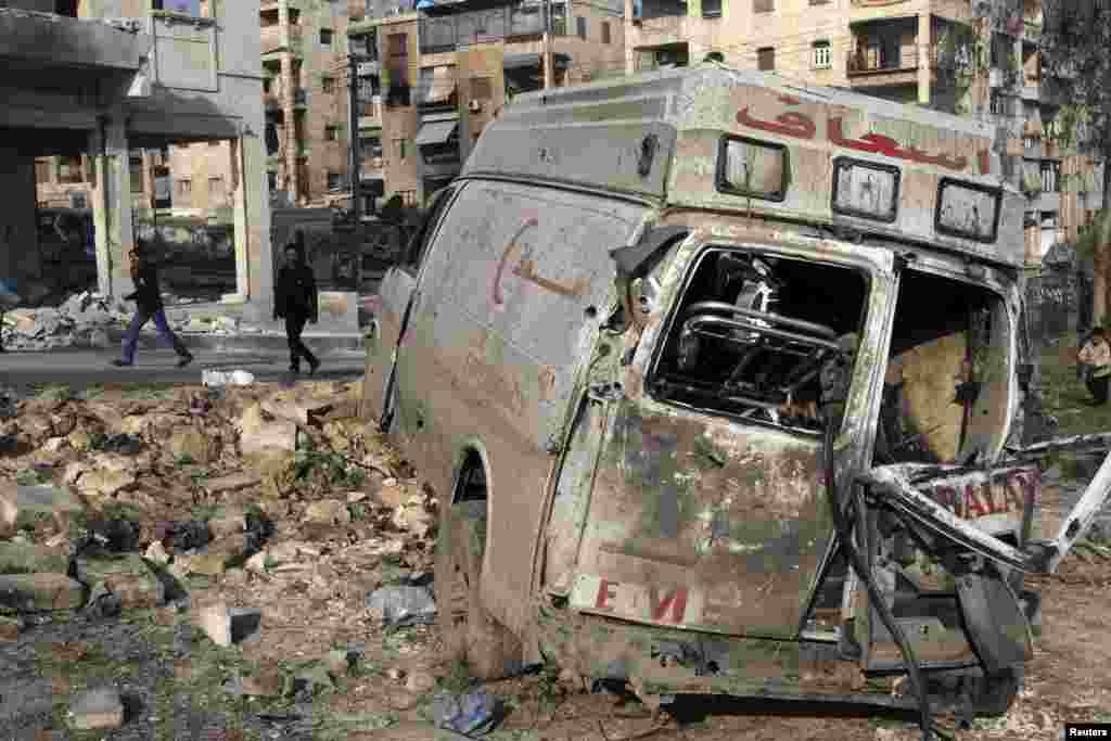 Residents walk past a damaged emergency vehicle in Aleppo, Syria, January 1, 2013.