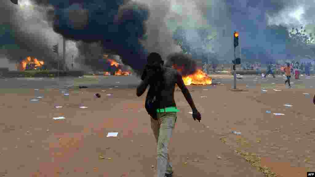 Un manifestant essuie son visage devant le parlement alors que des voitures et des documents brûlent à l'extérieur, à Ouagadougou le 30 octobre, 2014. Des centaines de manifestants en colère au Burkina Faso ont pris d'assaut le parlement le 30 Octobre avant d'y mettre le feu en signe de protestation contre l'intention de modifier la Constitution pour permettre au Président Blaise Compaoré pour étendre son règne de 27 ans. AFP PHOTO / ISSOUF SANOGO 