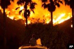 King Bass, 6, sits and watches a fire burn from on top of his parents' car as his sister Princess, 5, rests her head on his shoulder, Aug. 9, 2018 in Lake Elsinore, Calif.