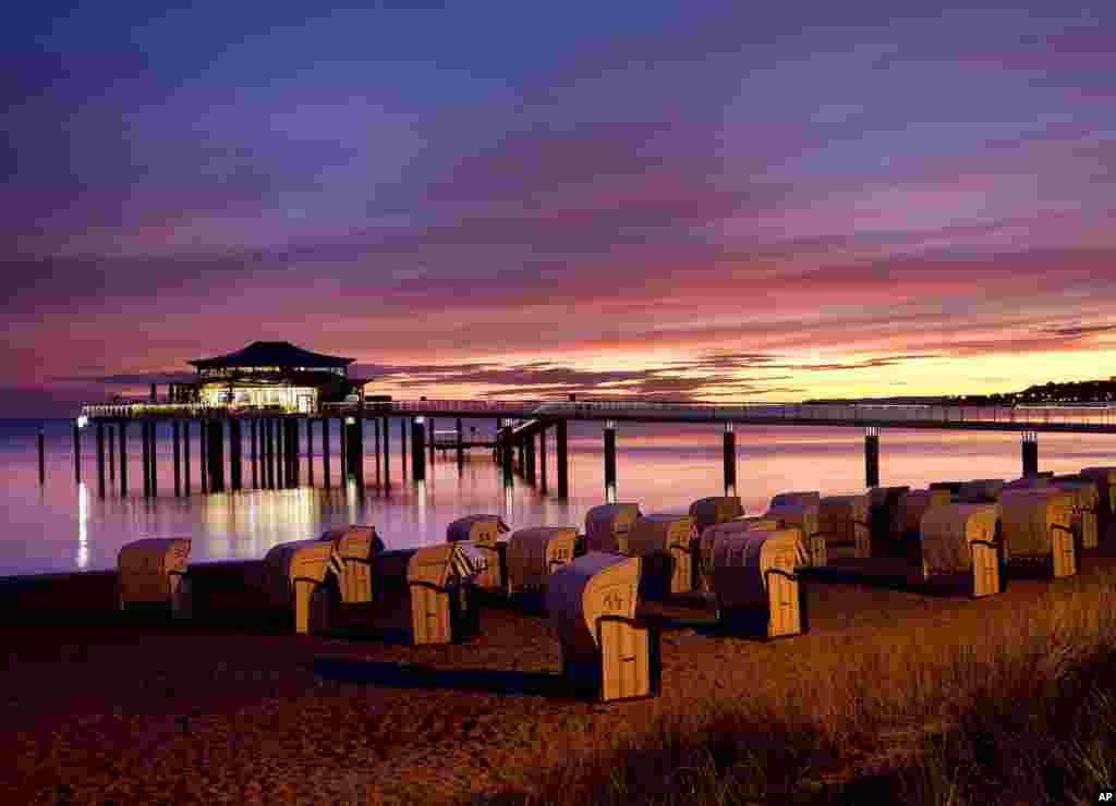 The sun is about to rise behind a sea bridge with a restaurant at the Baltic Sea in Timmendorfer Strand, Germany.
