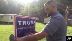 Billy Prater, 27, memperbaiki spanduk Donald Trump di pagar rumahnya di Beech Creek, West Virginia. Di-PHK dari tambang batu bara, ia menganggur selama lebih dari setahun sebelum bekerja di perusahaan kereta api.