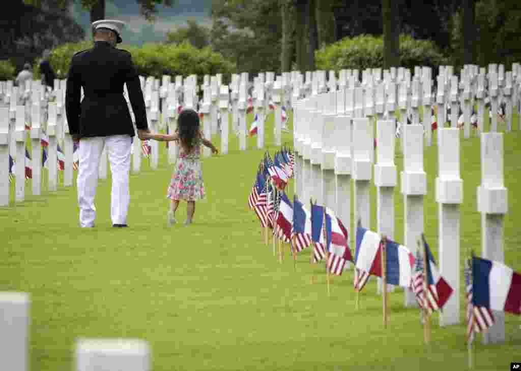 ទាហាន Marine Corps អាមេរិក​ដើរ​ជាមួយ​នឹង​ក្មេងស្រី​ម្នាក់​កាត់​ស្លាក​វិញ្ញាណក្ខន្ធ​មុន​ទិវា​រំឭក​វិញ្ញណក្ខន្ធ Memorial Day នៅ​កន្លែង​បញ្ចុះ​សព Aisne-Marne American Cemetery នៅ​ក្នុង​ក្រុង Belleau ប្រទេស​បារាំង។