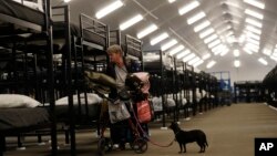 Verna Vasbinder prepares her new bunk in the city's new Temporary Bridge Shelter for the homeless as her dog, Lucy Lui, looks on, Dec. 1, 2017, in San Diego. The first of three shelters opened Friday, which will eventually provide beds for up to 700 people, as the city struggles to control a homeless crisis gripping the region.