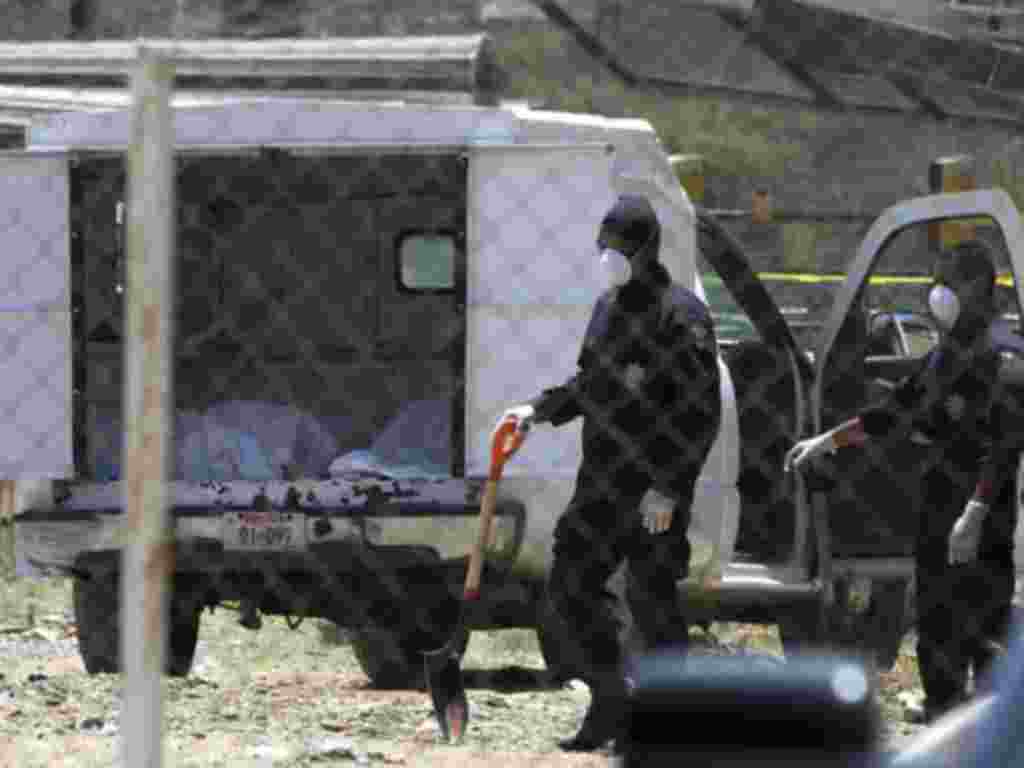Police stand near a coroner's car containing bodies found in a mass grave in Durango, April 20, 2011