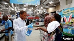 A store assistant gives people hand sanitiser as shoppers stock up on groceries at a Makro Store ahead of a nationwide 21 day lockdown in an attempt to contain the coronavirus disease (COVID-19) outbreak in Durban, South Africa, March 24, 2020.