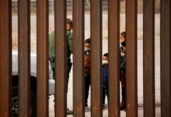 FILE - People are detained by a U.S. Border Patrol agent after crossing the Rio Bravo River to turn themselves in to request asylum in El Paso, Texas, as seen from Ciudad Juarez, Mexico, March 29, 2021.