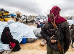 FILE - A member of Kurdish security forces watches as families load their belongings onto trucks before leaving the Kurdish-run al-Hol camp, in the Hasakah governorate in northeastern Syria, Nov. 16, 2020.